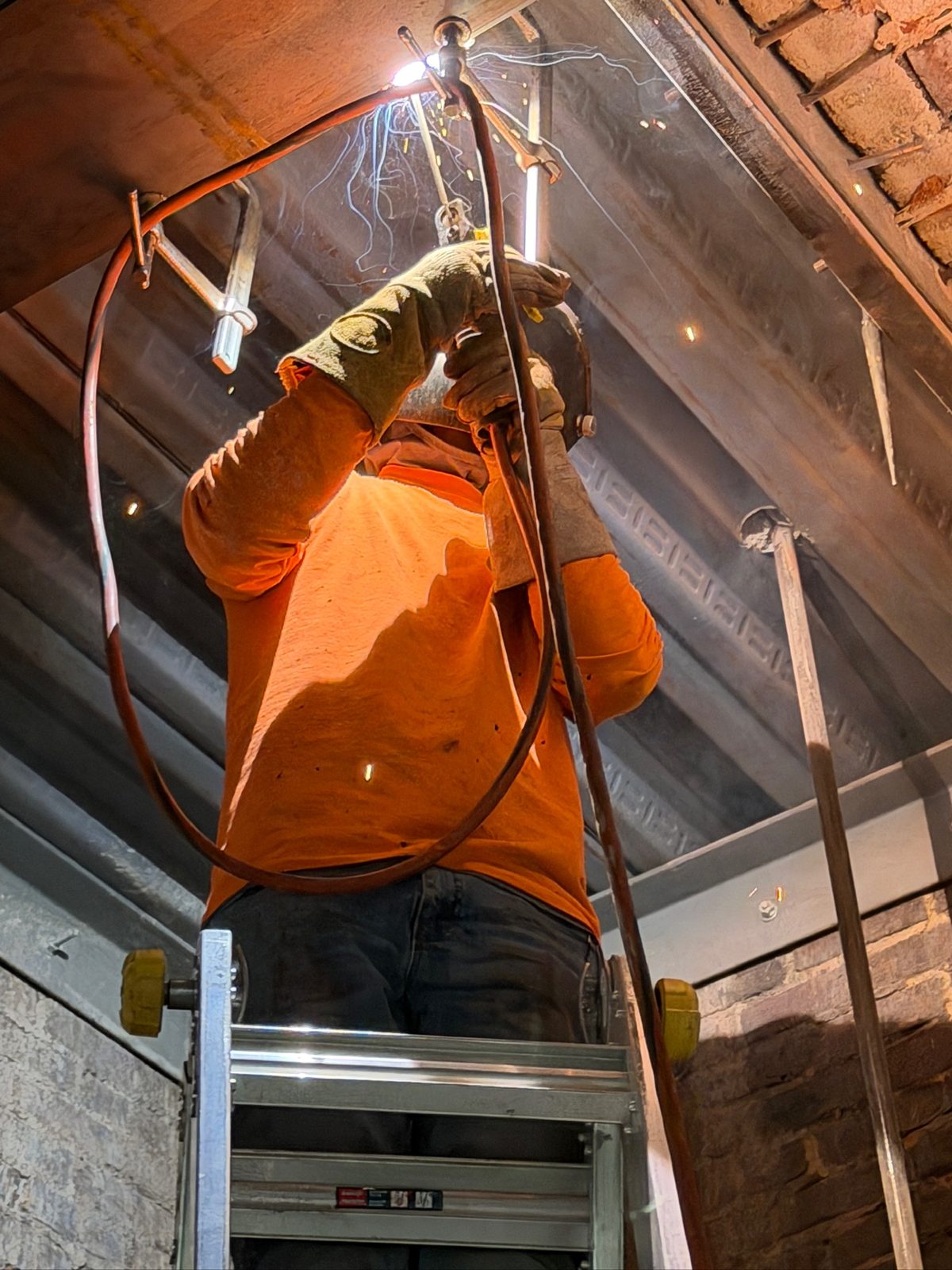 Overhead structural welding on steel reinforcement inside a custom fireplace enclosure at a high-end condominium.