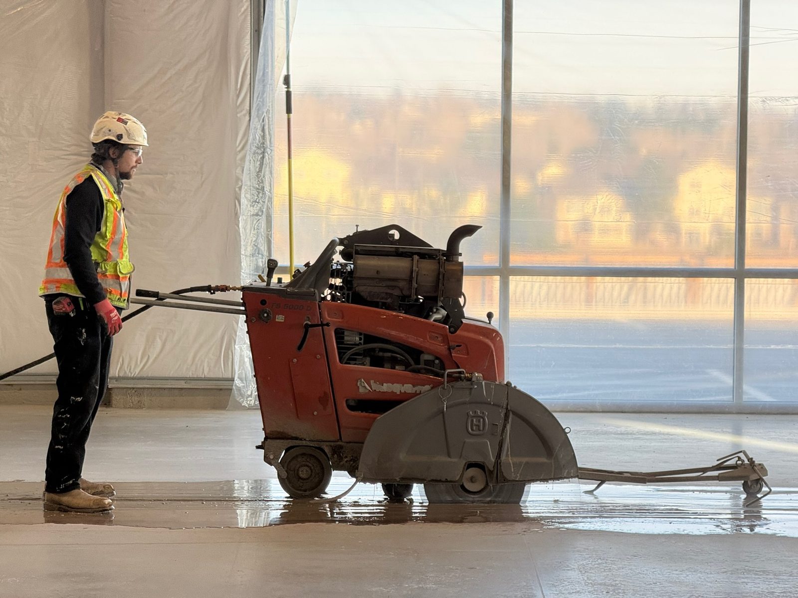 Trench cutting through a tilt-up warehouse slab, leaving straight wet-cut lines ready for the plumbing crew