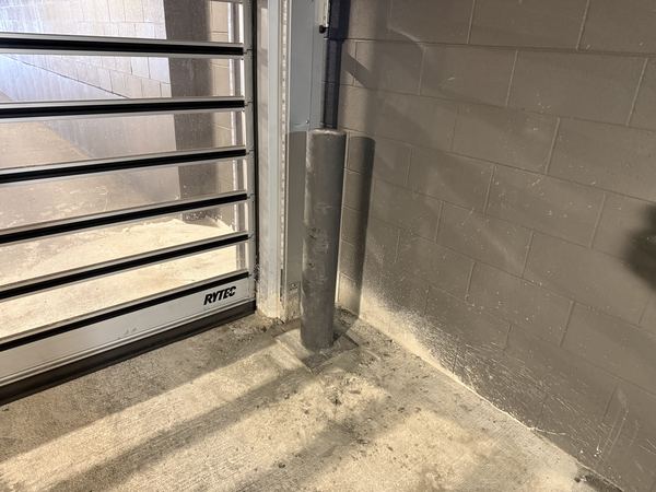 Galvanized steel bollard cored, set, and installed at a roll-up door track